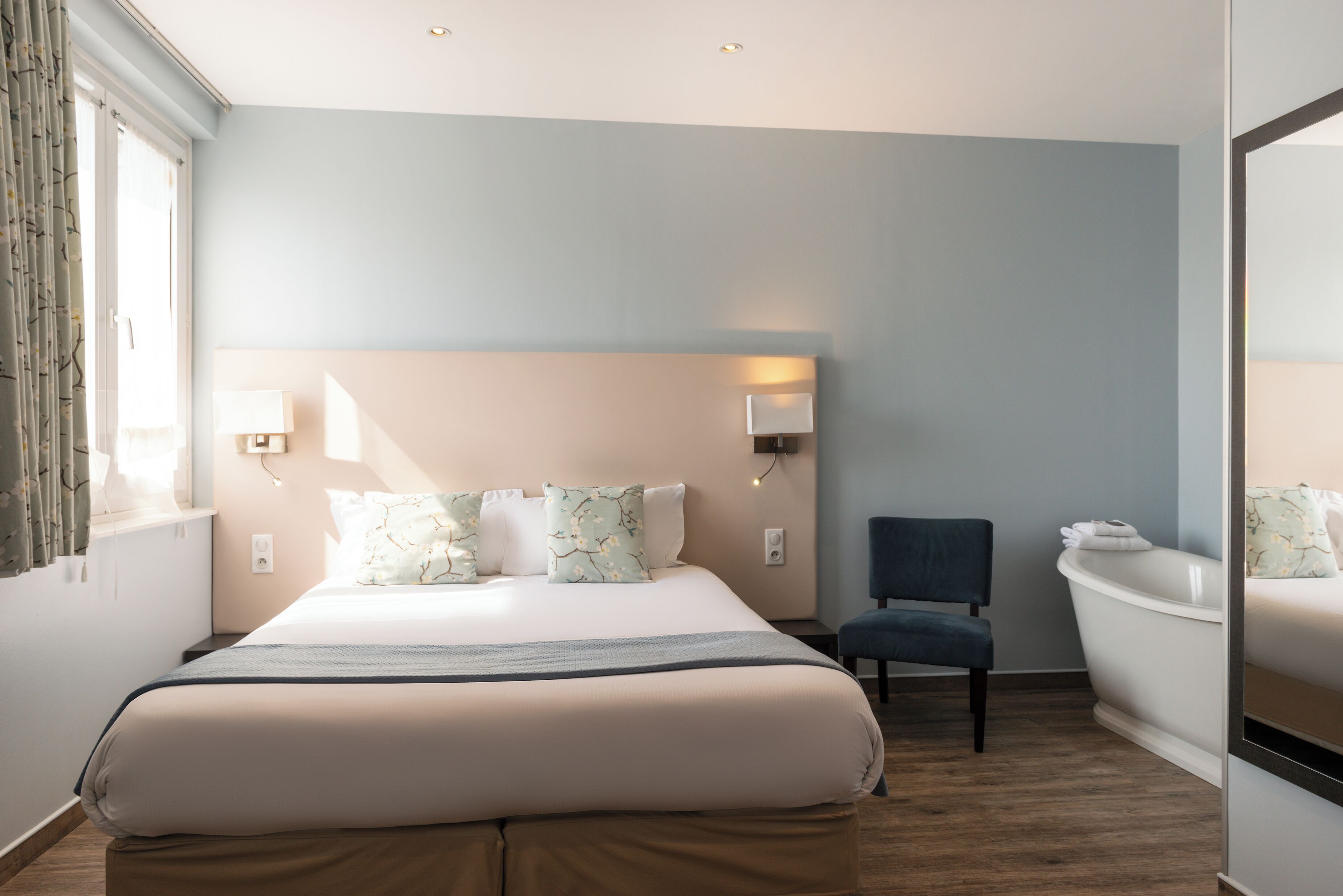 A hotel room with a large bed, bedside lamps, a chair, and a bathtub.