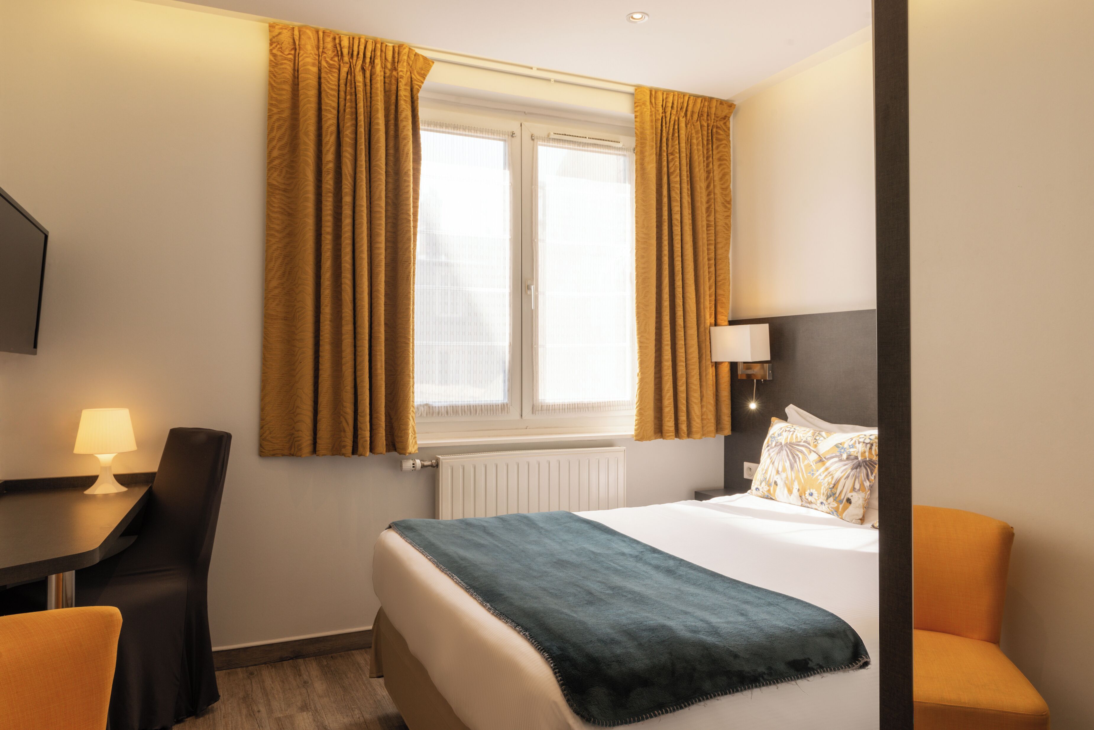 A hotel room with a bed, a desk, a chair, and a window with curtains.