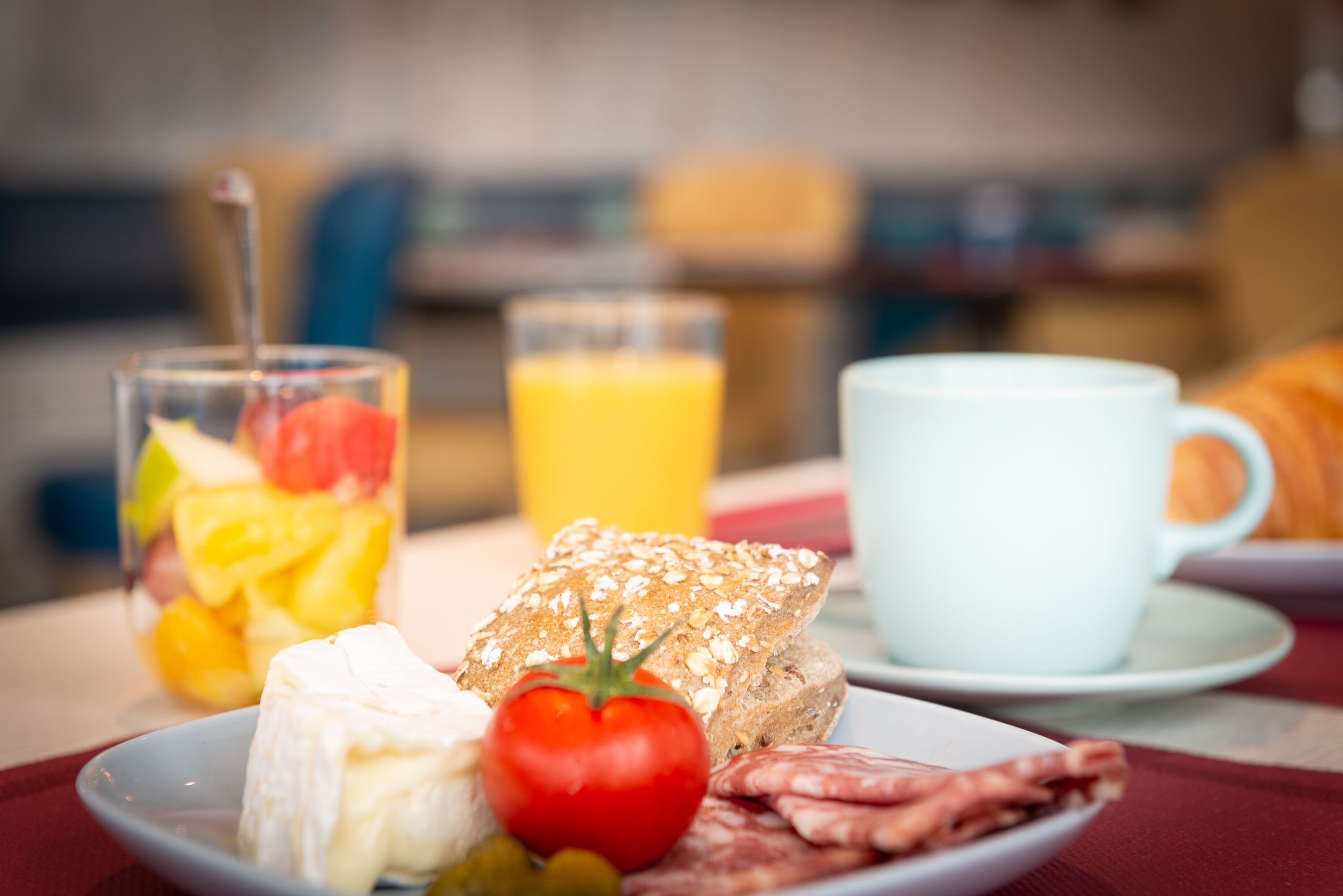 Une table mise pour le petit-déjeuner, avec une assiette de nourriture, un verre de jus d’orange et une tasse blanche.