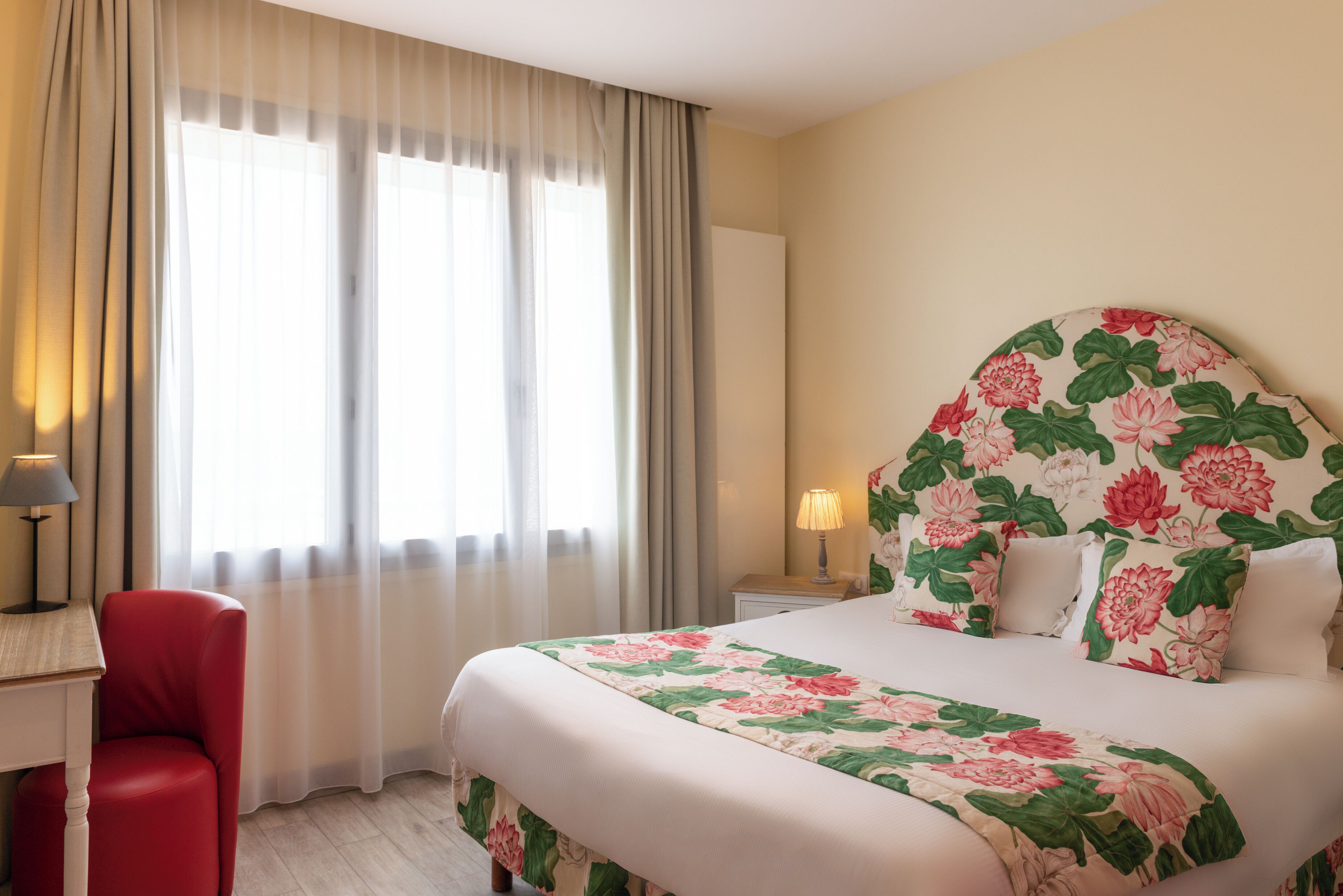 Habitación de hotel con una cama grande, una silla roja, un escritorio y una mesita de noche con una lámpara.