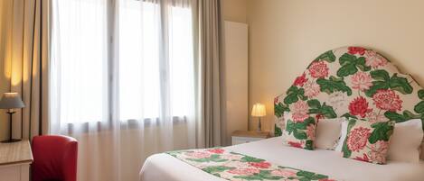 Habitación de hotel con una cama grande, una silla roja, un escritorio y una mesita de noche con una lámpara.