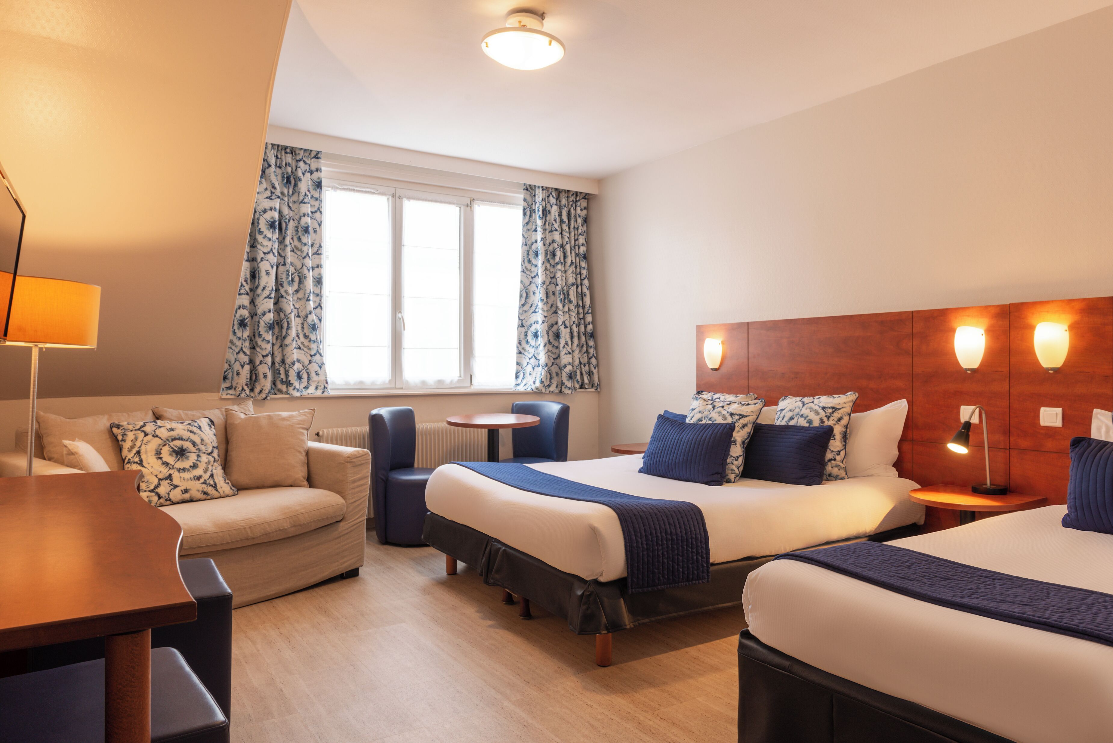 Una habitación de hotel con una cama, un sofá, una mesita y una lámpara.