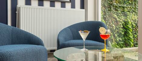 A modern living room with a large window, a blue sofa, a glass coffee table with drinks, and a poster on the wall.