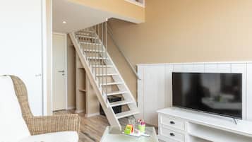 A living room with a glass coffee table, wicker furniture, a flat-screen TV, and a staircase.