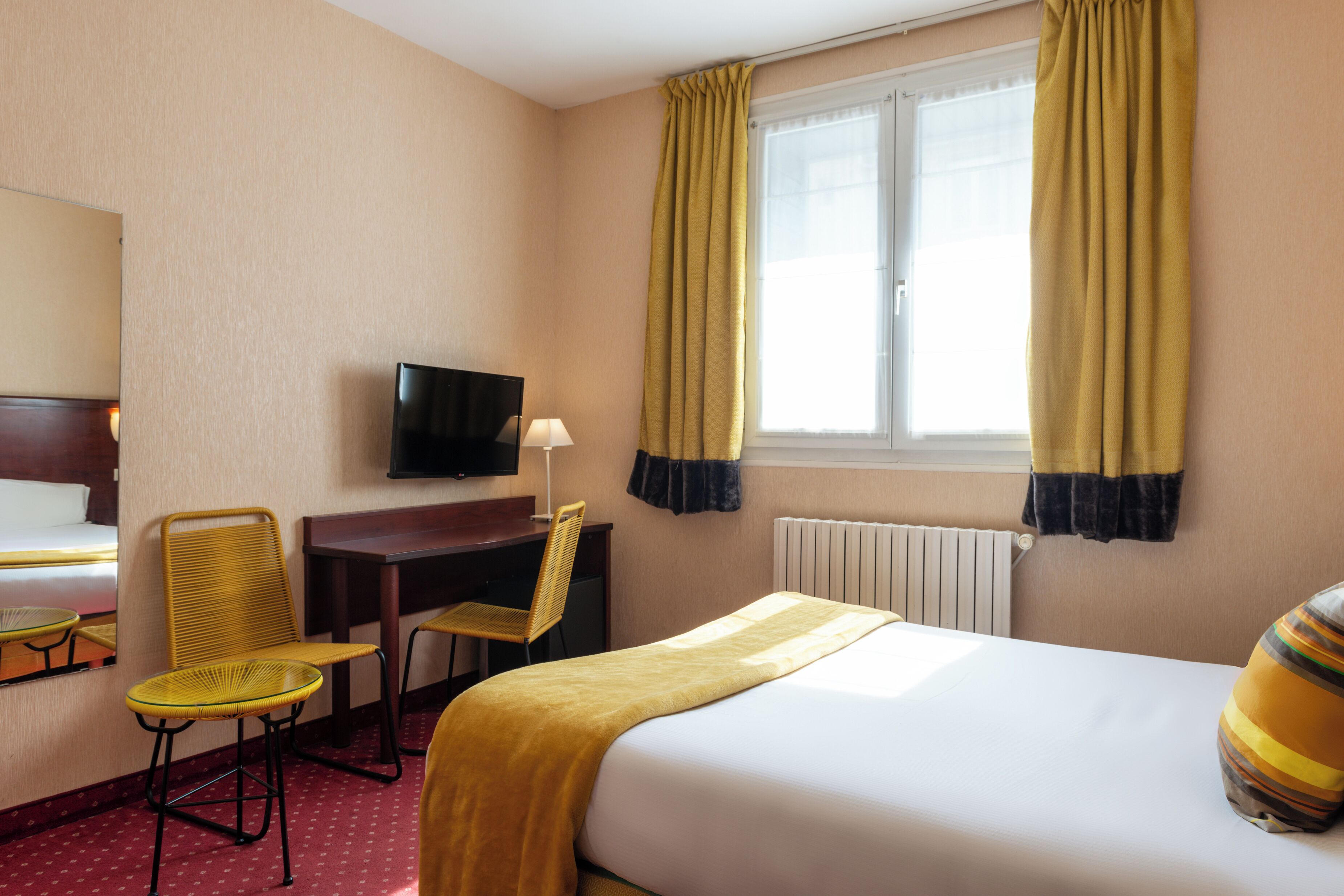 Habitación de hotel con cama, escritorio, silla, televisor y ventana con cortinas.