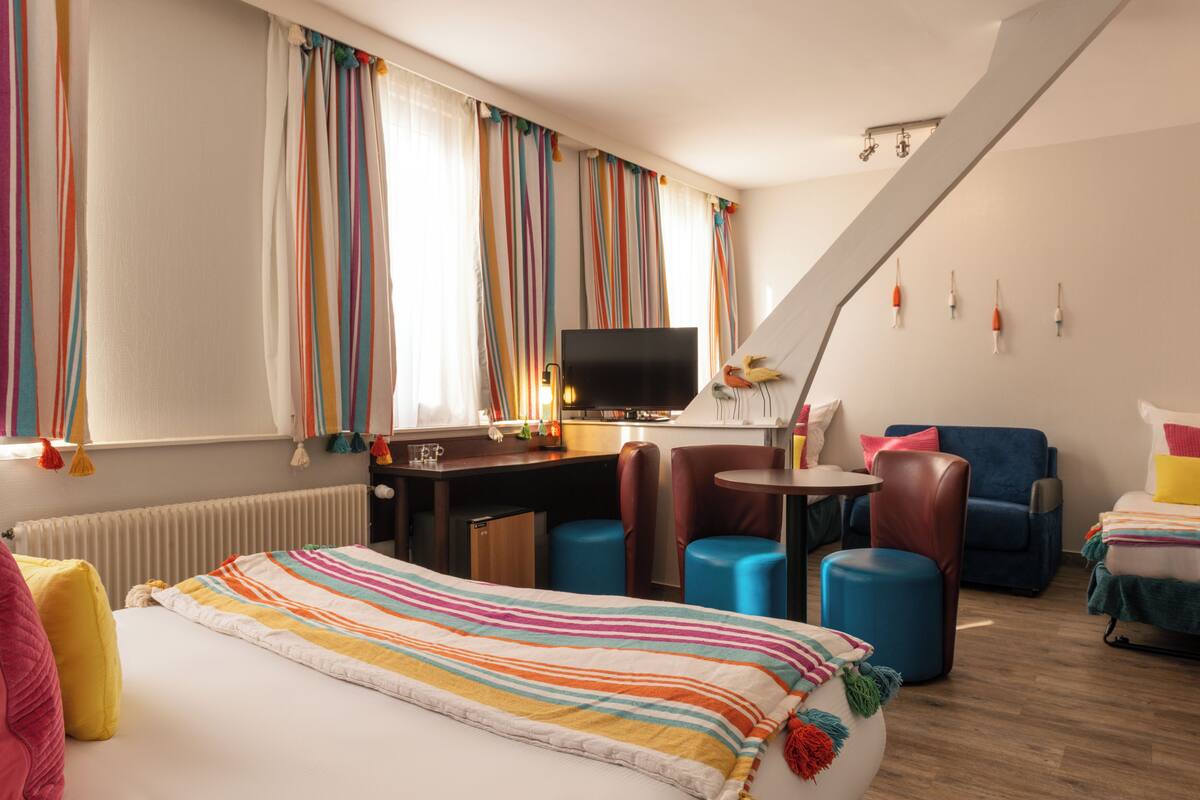 A hotel room with a bed, a desk, a TV, a chair, and a small table.