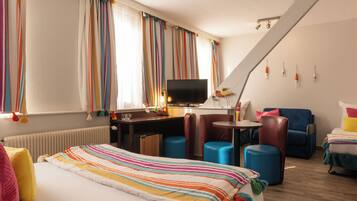 Habitación de hotel con cama, escritorio, televisión, silla y una mesita.