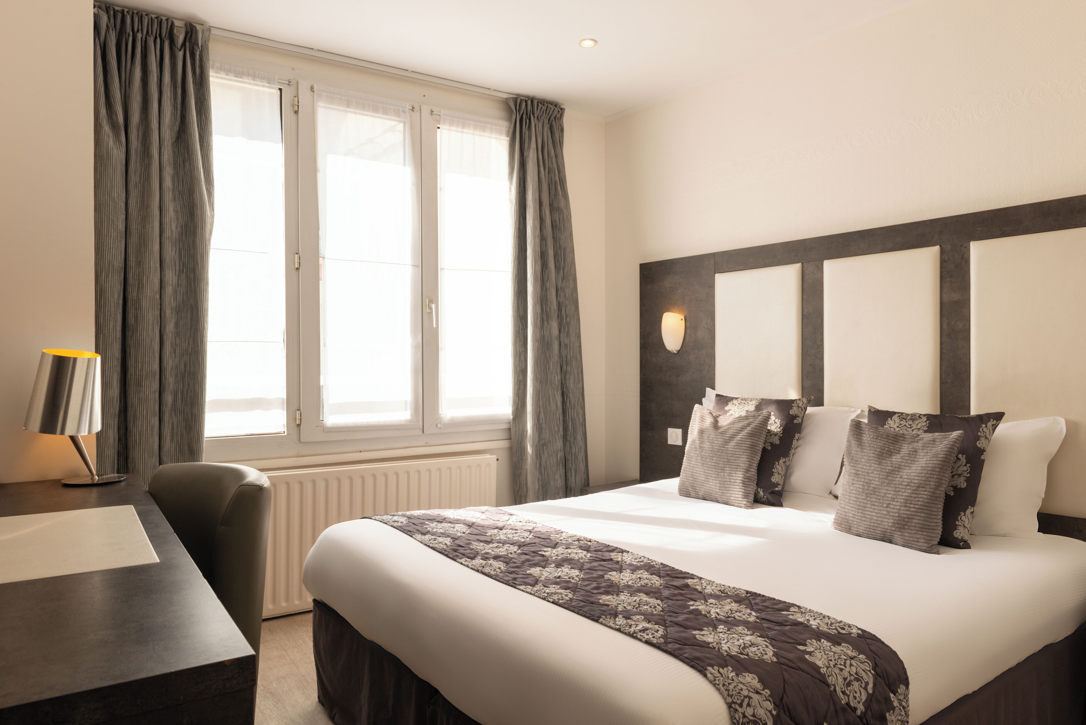 A hotel room with a large bed, a desk, and a window with curtains.