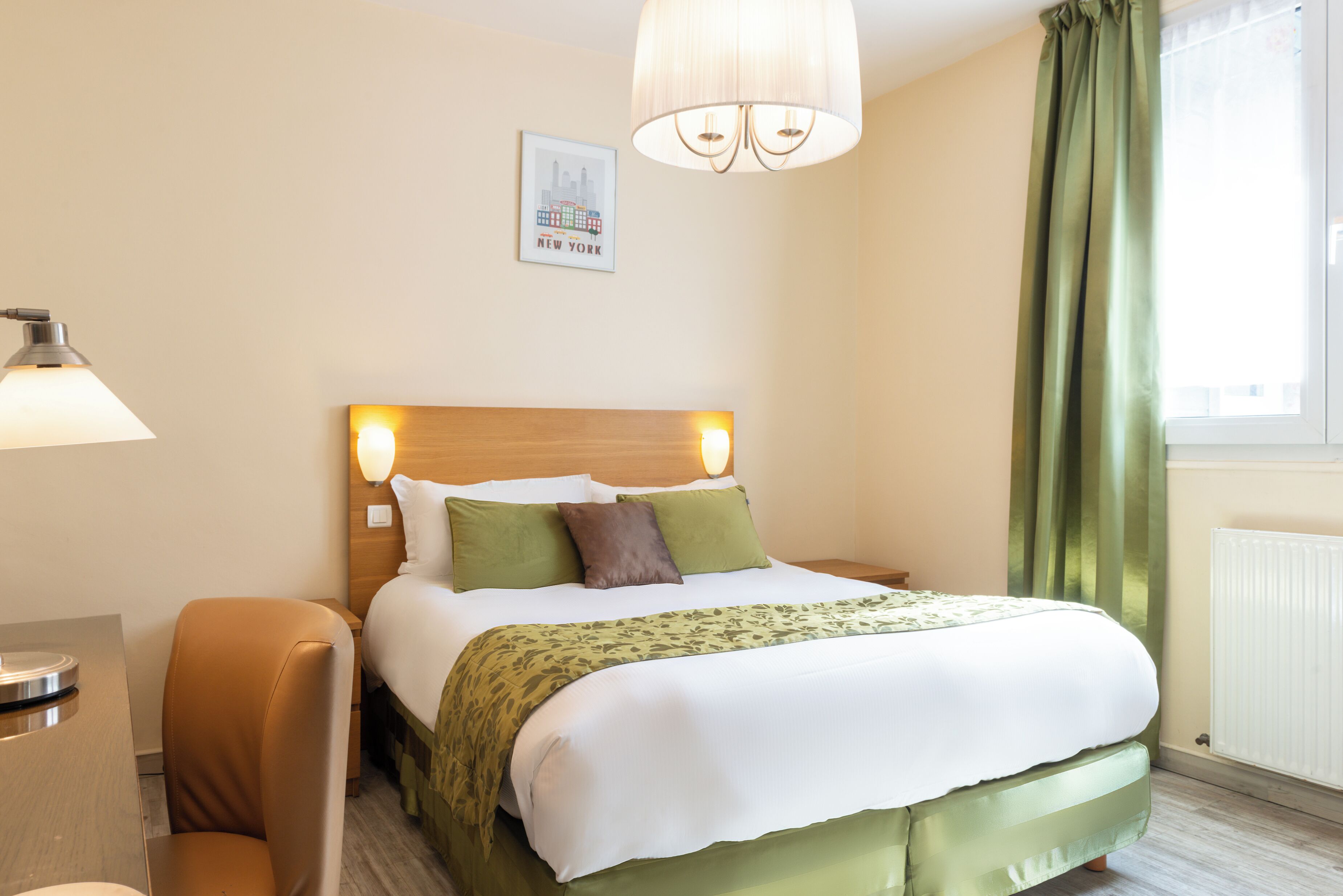 A hotel room with a bed, a chair, a lamp, and a window with curtains.