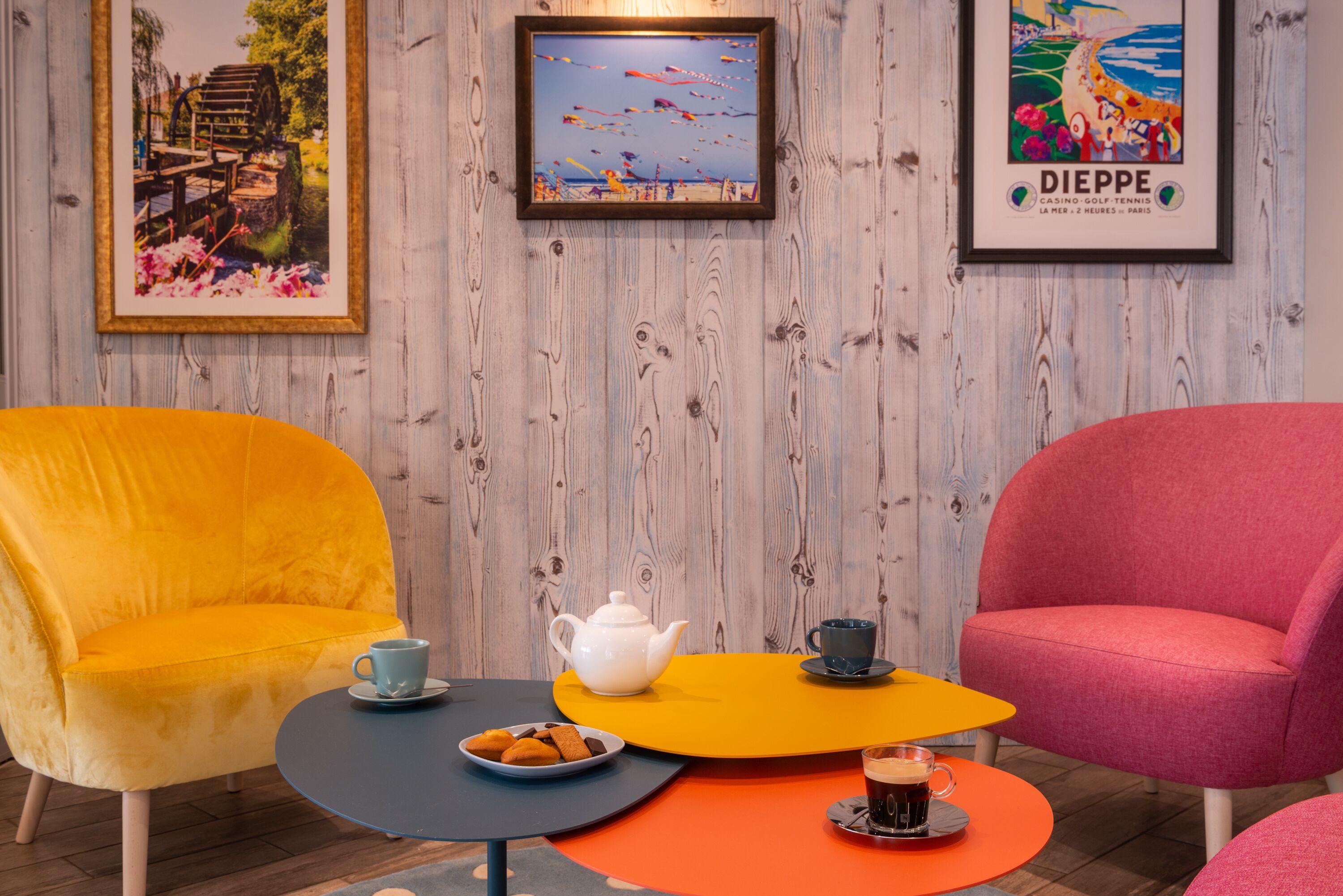 Un coin salon accueillant avec deux fauteuils aux couleurs vives, une petite table sur laquelle se trouvent une théière, des tasses et une assiette de biscuits.