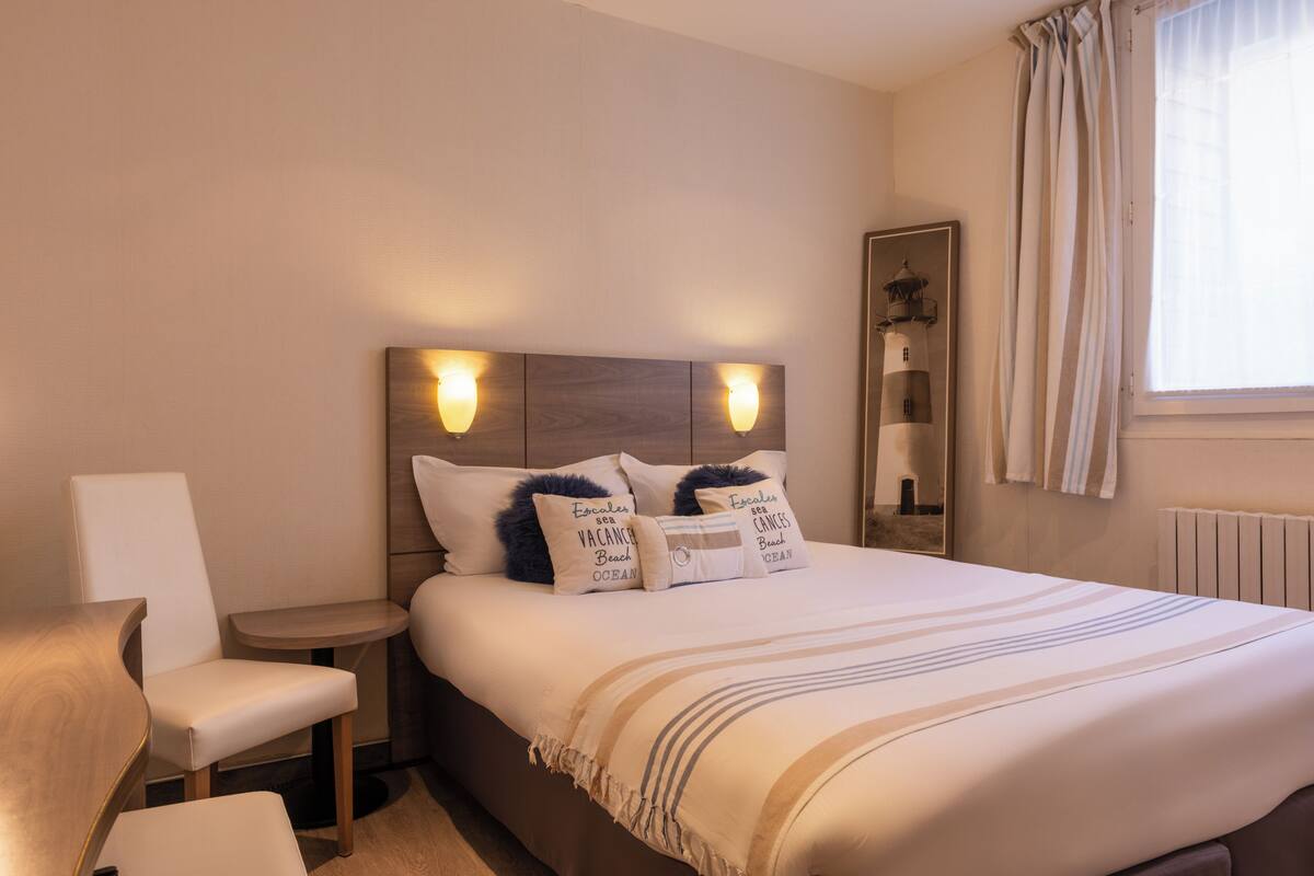 A neatly arranged hotel room with a large bed, two bedside tables, a chair, and a window with curtains.