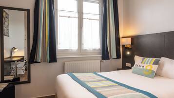 A hotel room with a large bed, a bedside table with a lamp, a mirror, and a window with curtains.