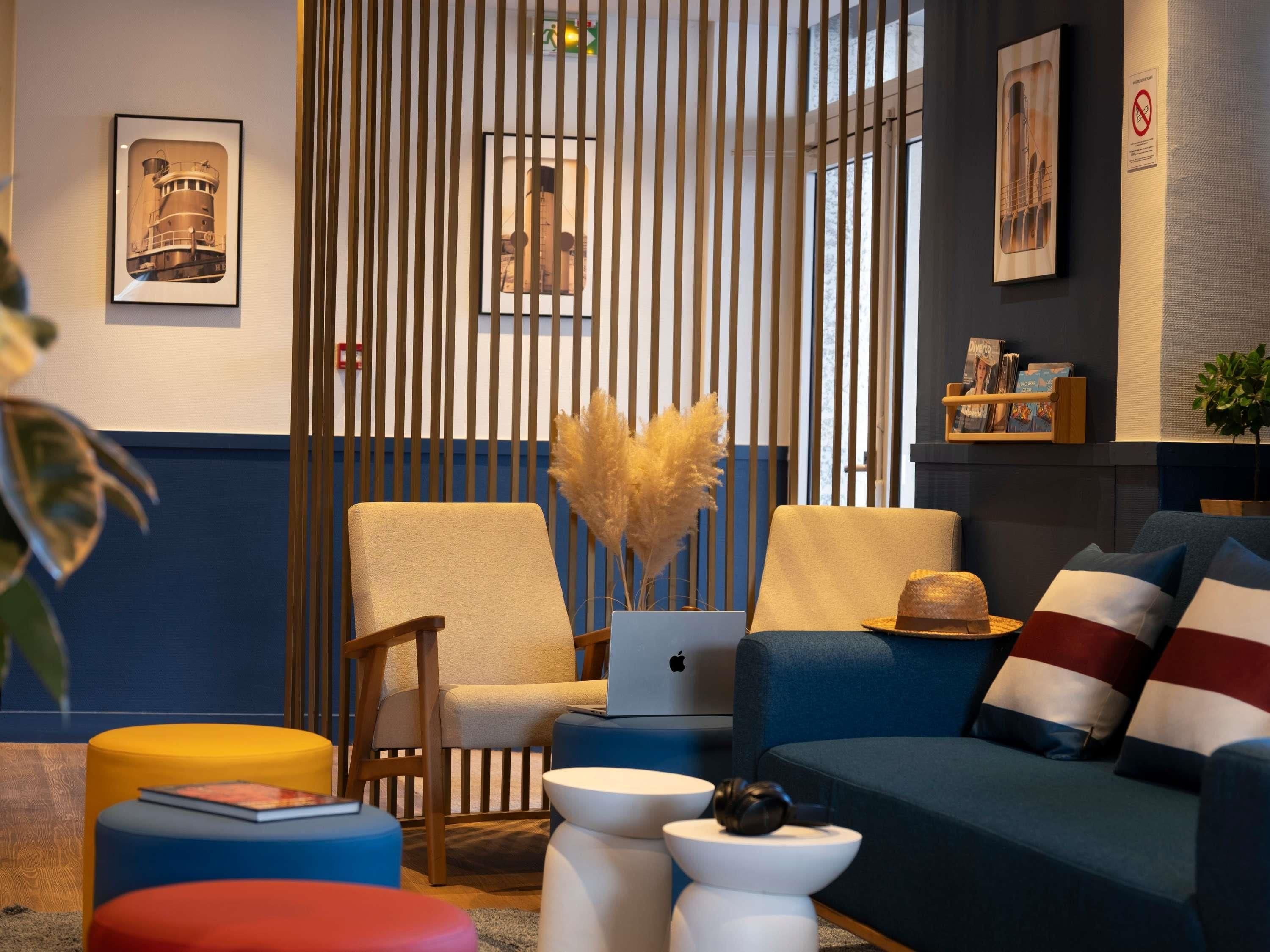 A modern living room with a blue sofa, a wooden chair, a laptop, and a decorative vase.