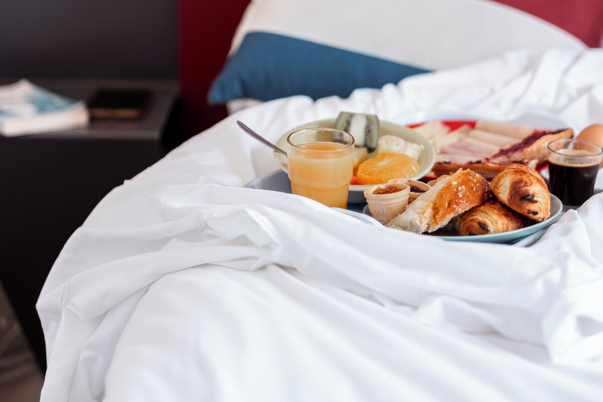 Una cama bien hecha con un carrito de desayuno que incluye croissants, jugo de naranja y una taza de café.
