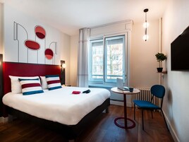 Habitación de hotel moderna con una cama grande, una mesita con una computadora portátil, una silla y vistas a la ciudad a través de la ventana.