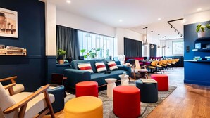 Ein moderner Loungebereich mit einer Couch, Poufs und einem Essbereich mit Stühlen und Tischen.