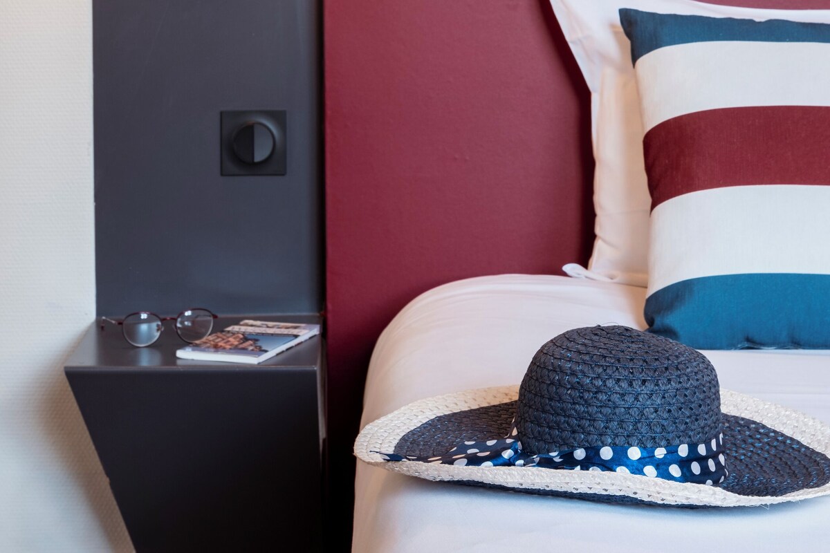 Una cama bien hecha con un almohadón a rayas y un sombrero tejido encima.