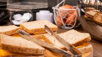 A wooden cutting board with a sandwich cut in half, a knife, and a basket of oranges in the background.
