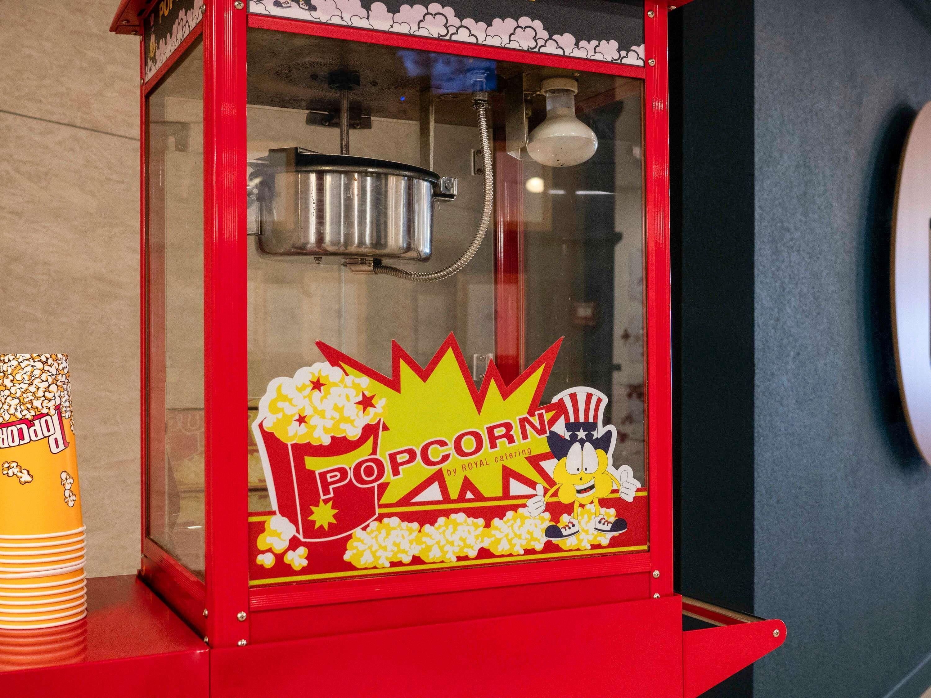Une machine à pop-corn rouge, ornée d’un personnage de dessin animé, avec les inscriptions « POP CORN » et « SERVICE TRAITEUR ROYAL par Hooters ».