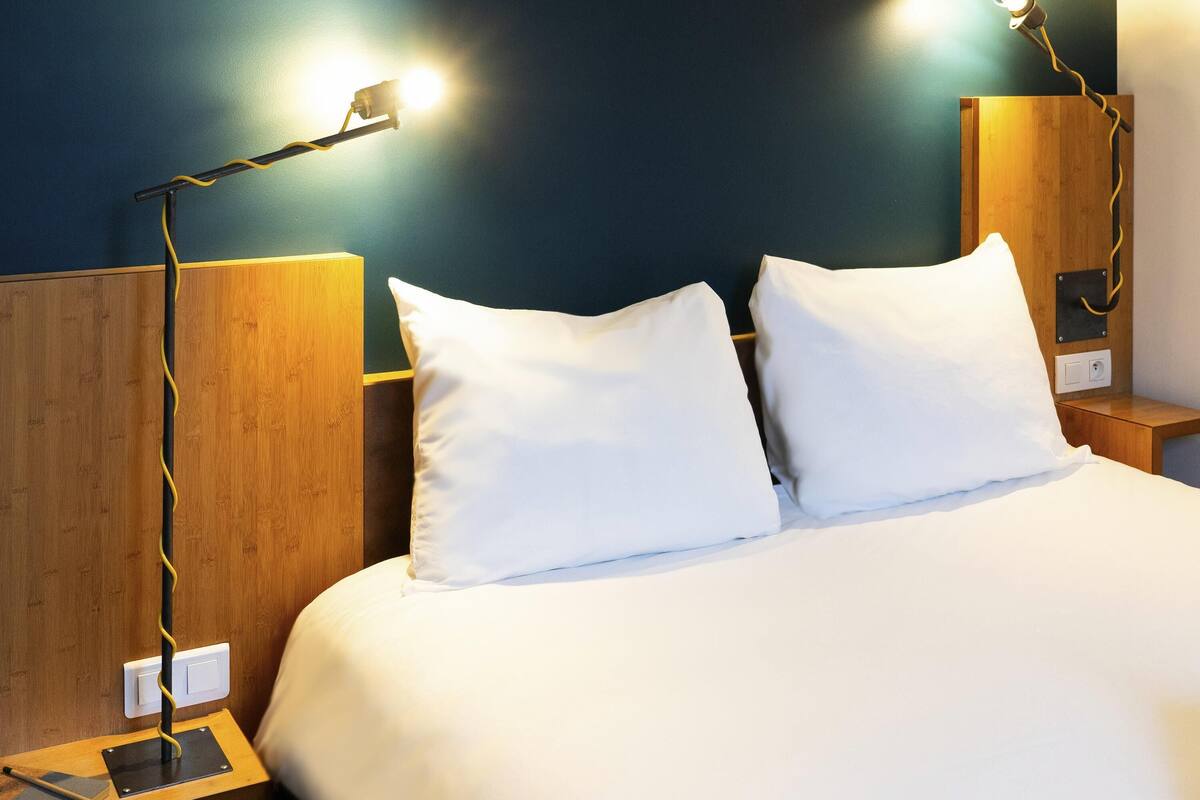 Ein ordentlich gemachtes Bett mit weißen Leinentüchern, zwei Nachttische mit Lampen und ein Holzkopfteil.