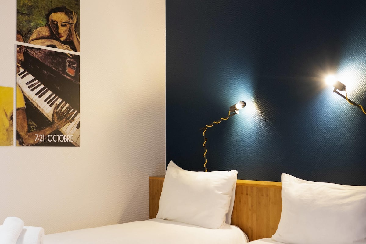 A hotel room with a bed, pillows, a poster, and a wall-mounted lamp.