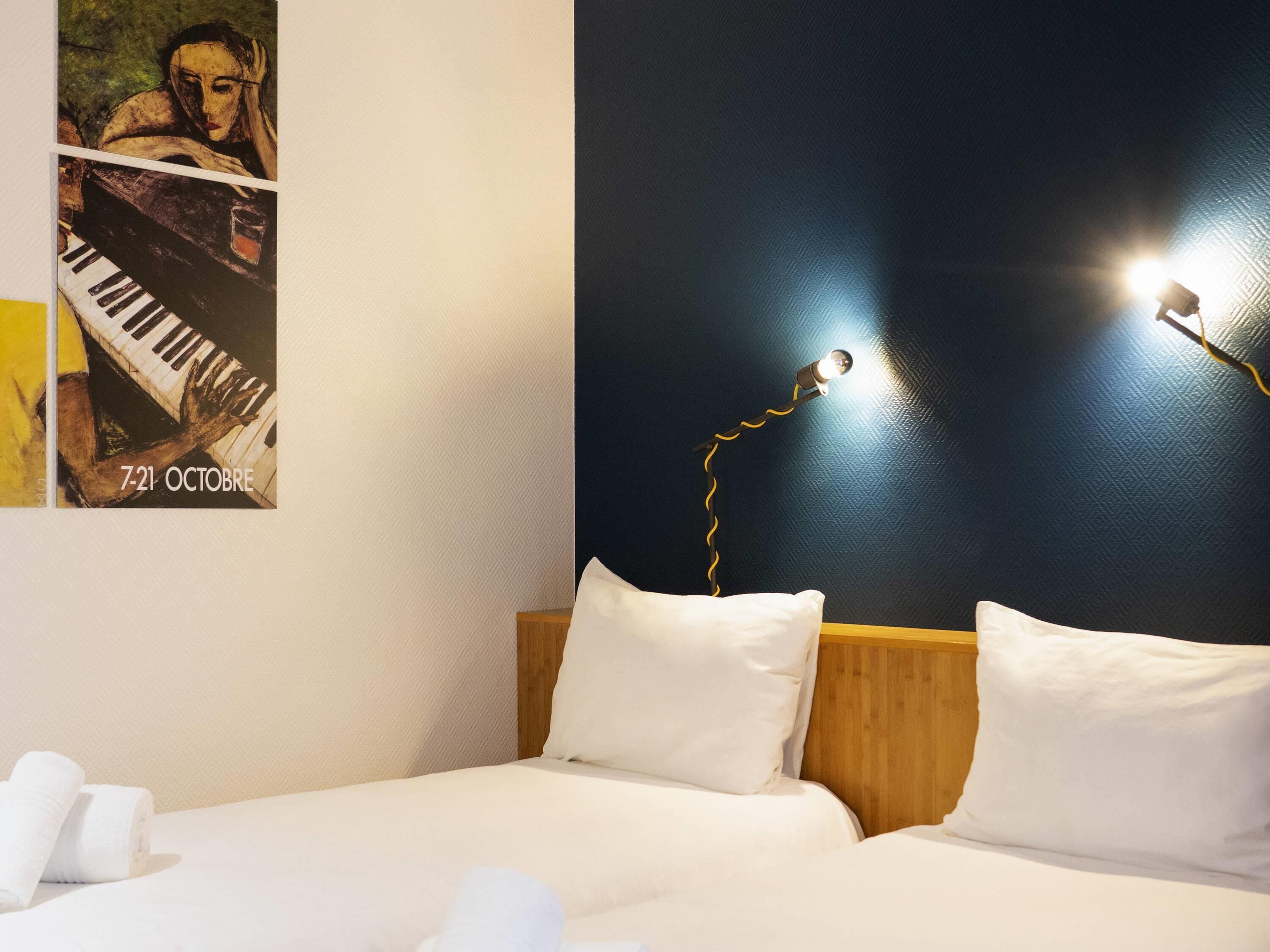 Une chambre d’hôtel avec un lit, des oreillers, une affiche et une lampe fixée au mur.