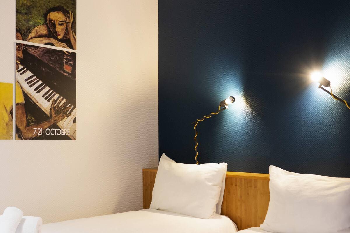 Une chambre d’hôtel avec un lit, des oreillers, une affiche et une lampe fixée au mur.