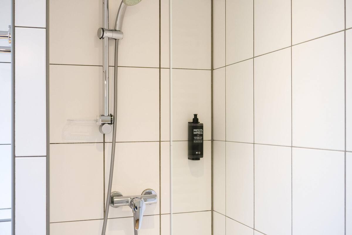 A shower with a handheld showerhead and a wall-mounted faucet.