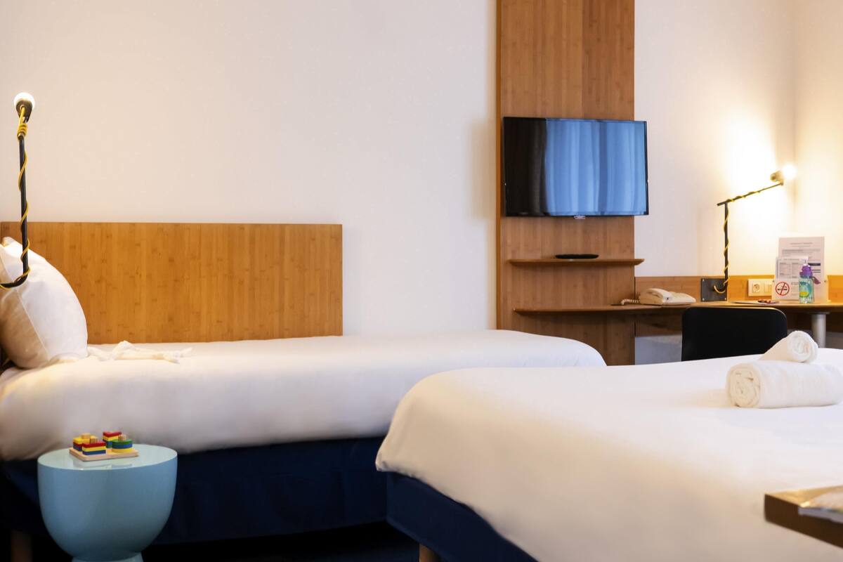Ein Hotelzimmer mit zwei Betten, einem Schreibtisch, einem Fernseher und einem kleinen runden Tisch mit einem Spielzeug.