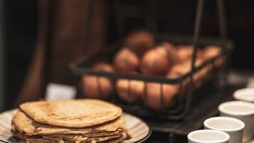 Una pila de tortitas en un plato, una bandeja de huevos y una fila de tazas blancas sobre una mesa.