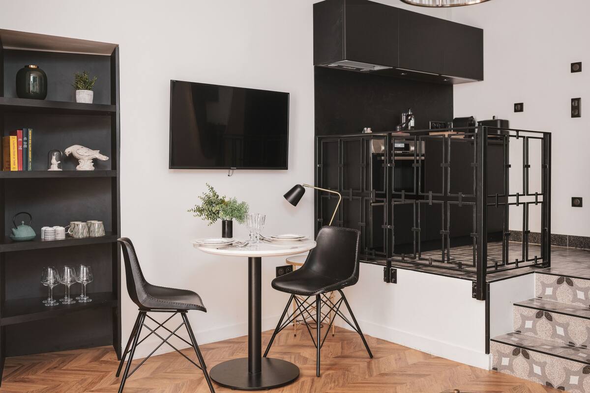 A modern kitchen with a black stove, a flat-screen TV, and a dining area with two chairs and a table.