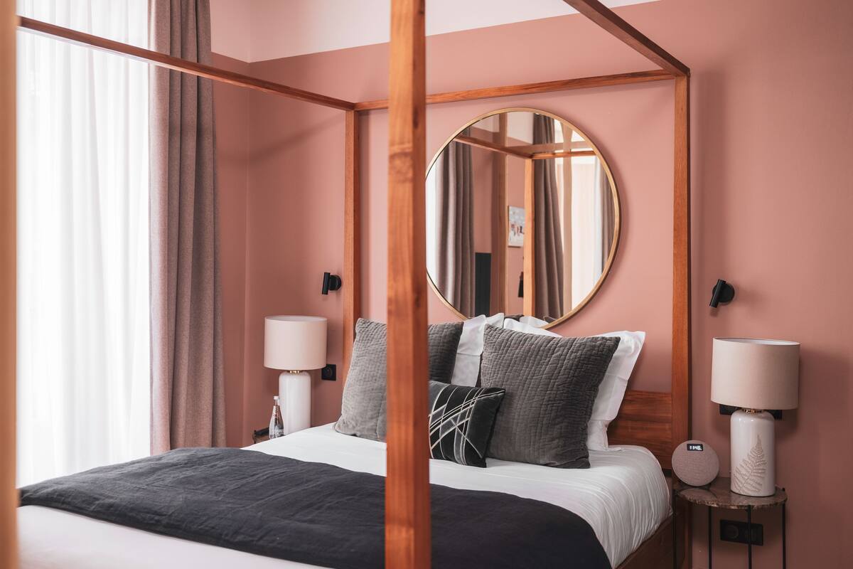 A four-poster bed with a round mirror above it, two bedside tables with lamps, and a view of the room's interior.