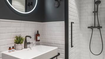 A modern bathroom with a white sink, black fixtures, a round mirror, and a shower area.