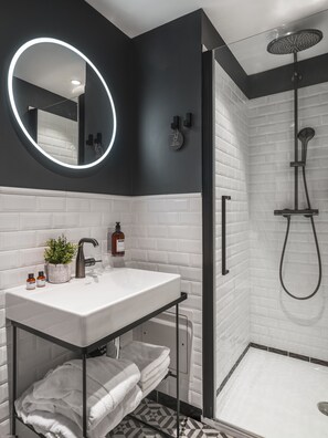 A modern bathroom with a white sink, black fixtures, a round mirror, and a shower area. - Maisons du Monde Hôtel & Suites - Nantes (Nantes)
