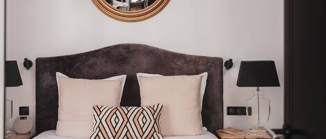 A neatly made bed with a dark headboard, two bedside lamps, and a round mirror on the wall.