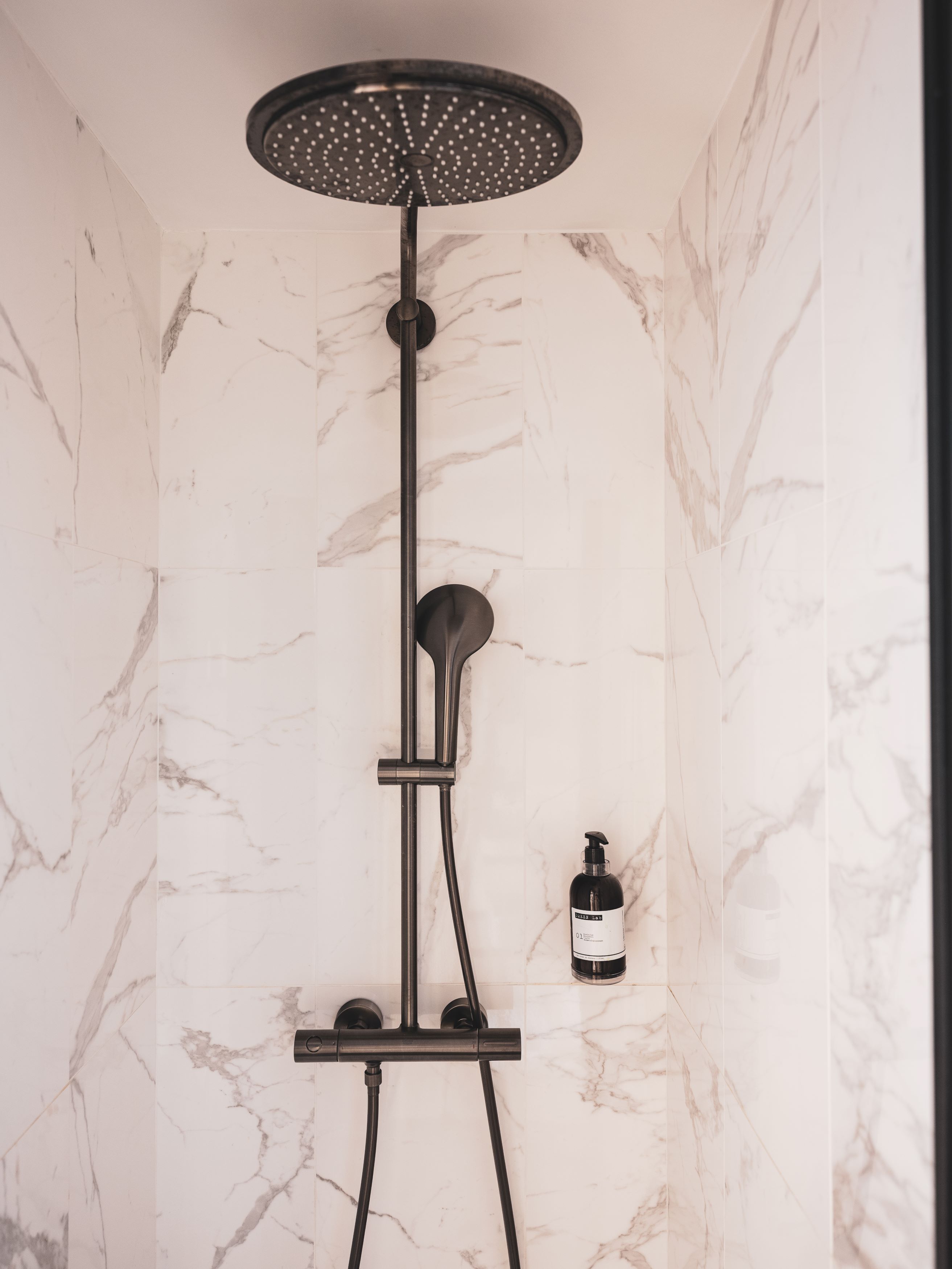 A modern shower with a rain showerhead, handheld showerhead, and a handheld shower attachment.