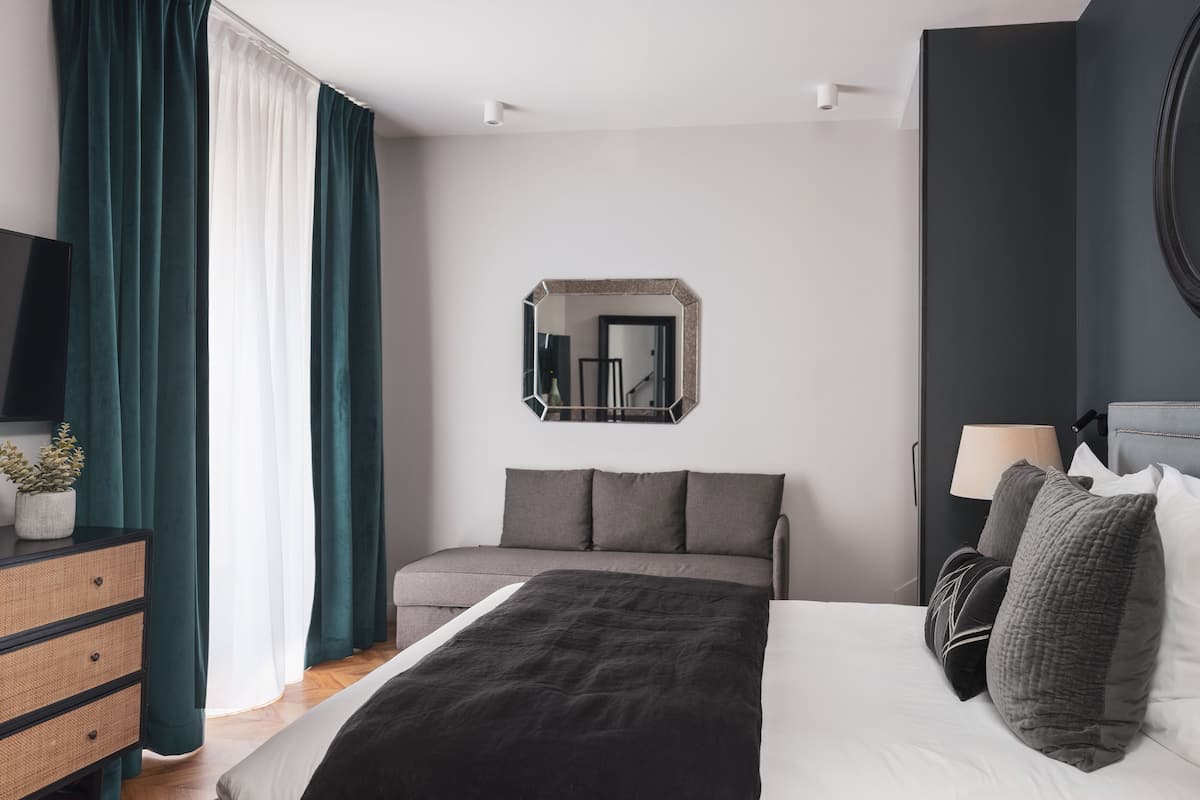 A modern bedroom with a bed, a dresser, a mirror, and a lamp.