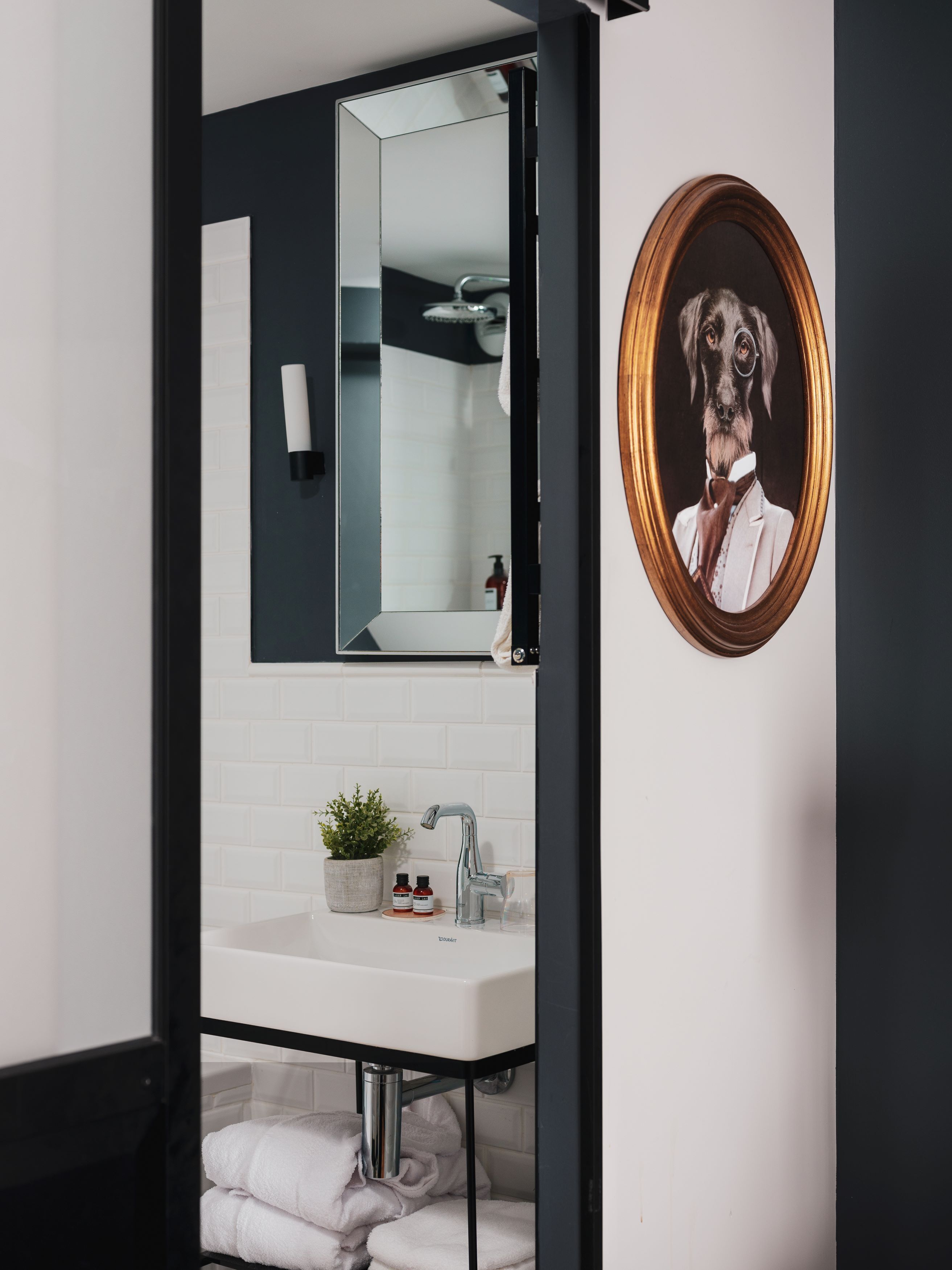 Uma casa de banho moderna com toucador preto, lavatório branco e um quadro com a imagem de um cão a usar fato.