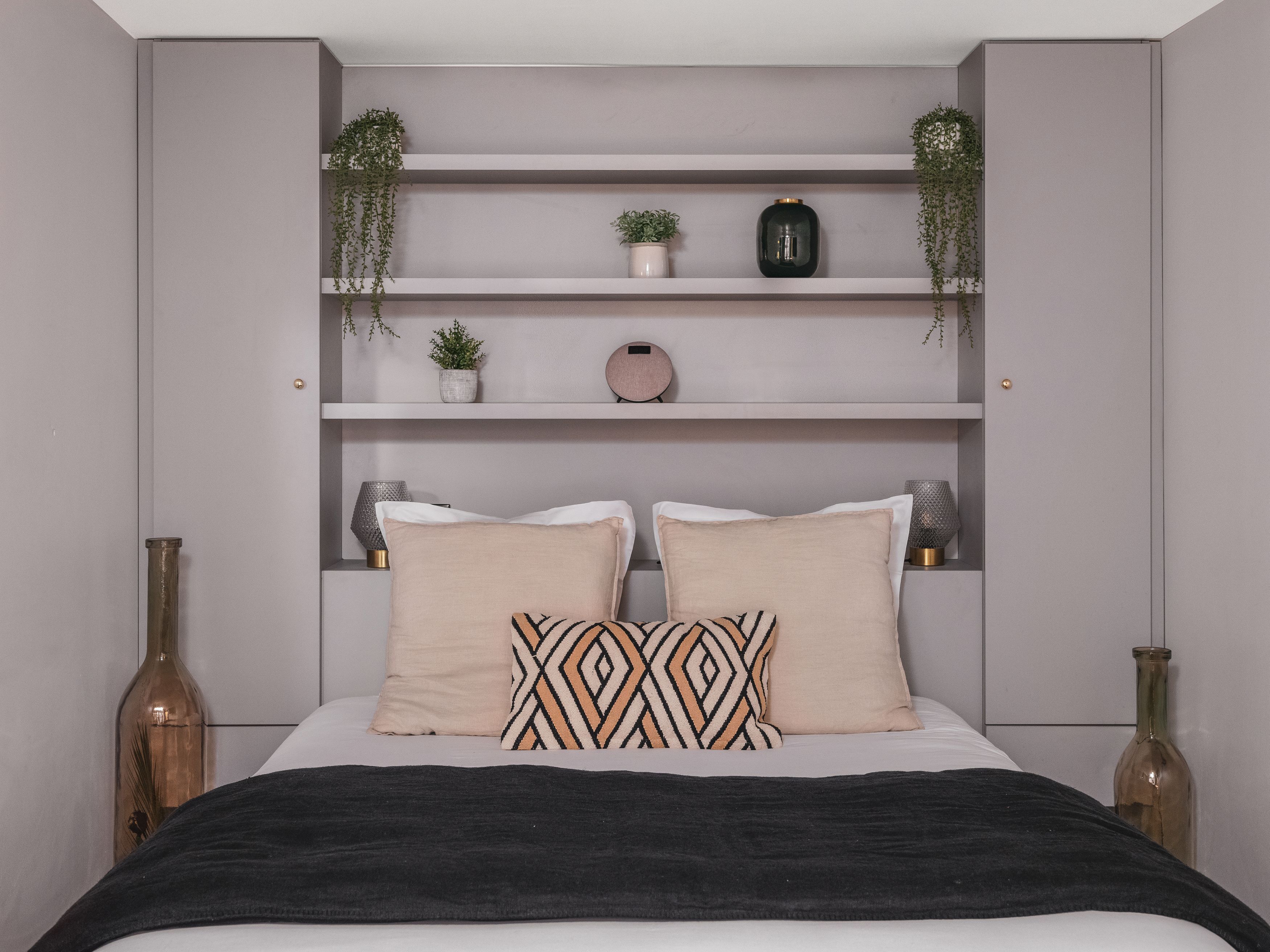 A bedroom with a bed, two bedside tables, a shelf with plants, and decorative items.