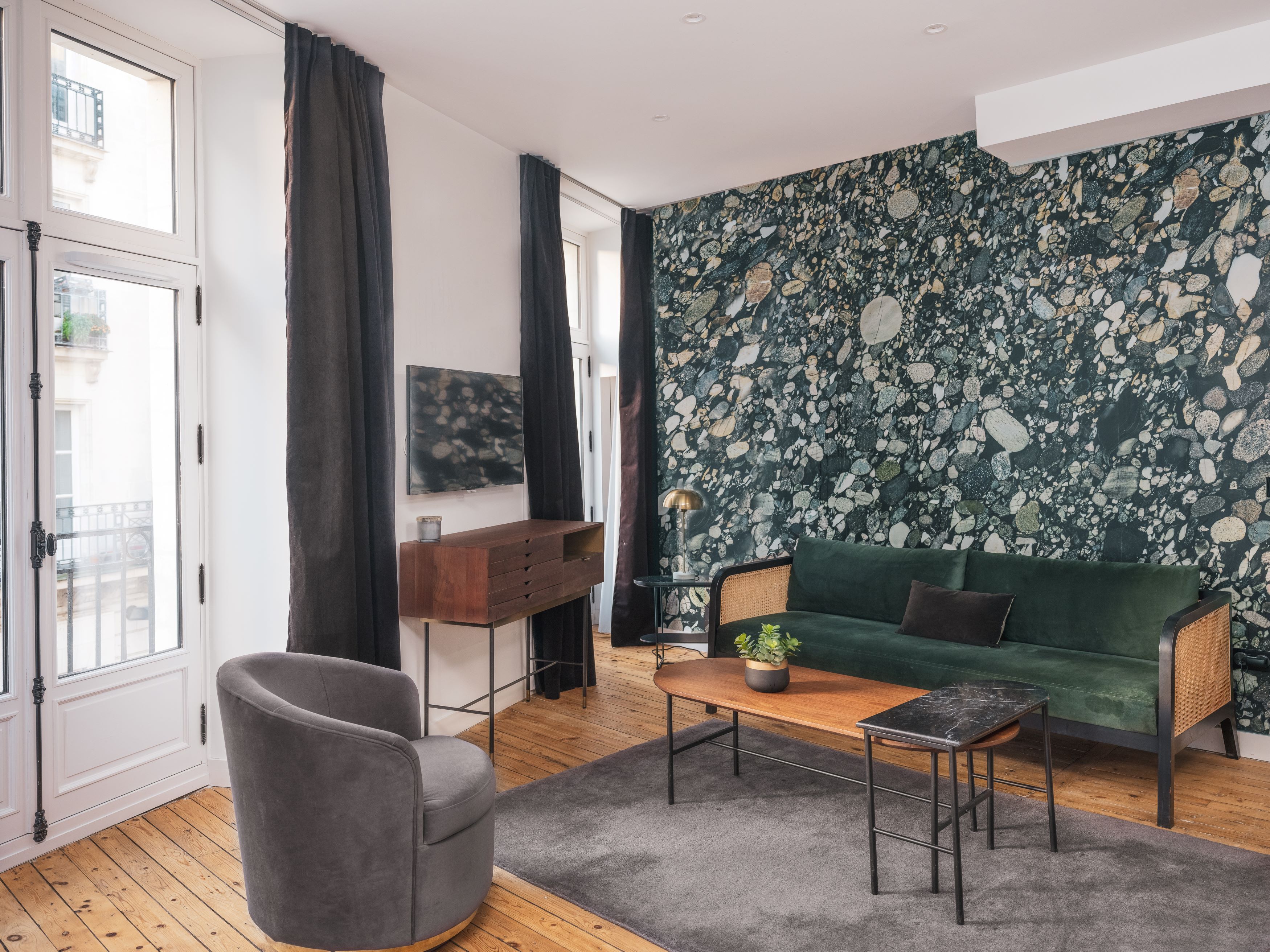 Un salon moderne avec un canapé vert, un fauteuil gris, une table basse en bois et un téléviseur fixé au mur.
