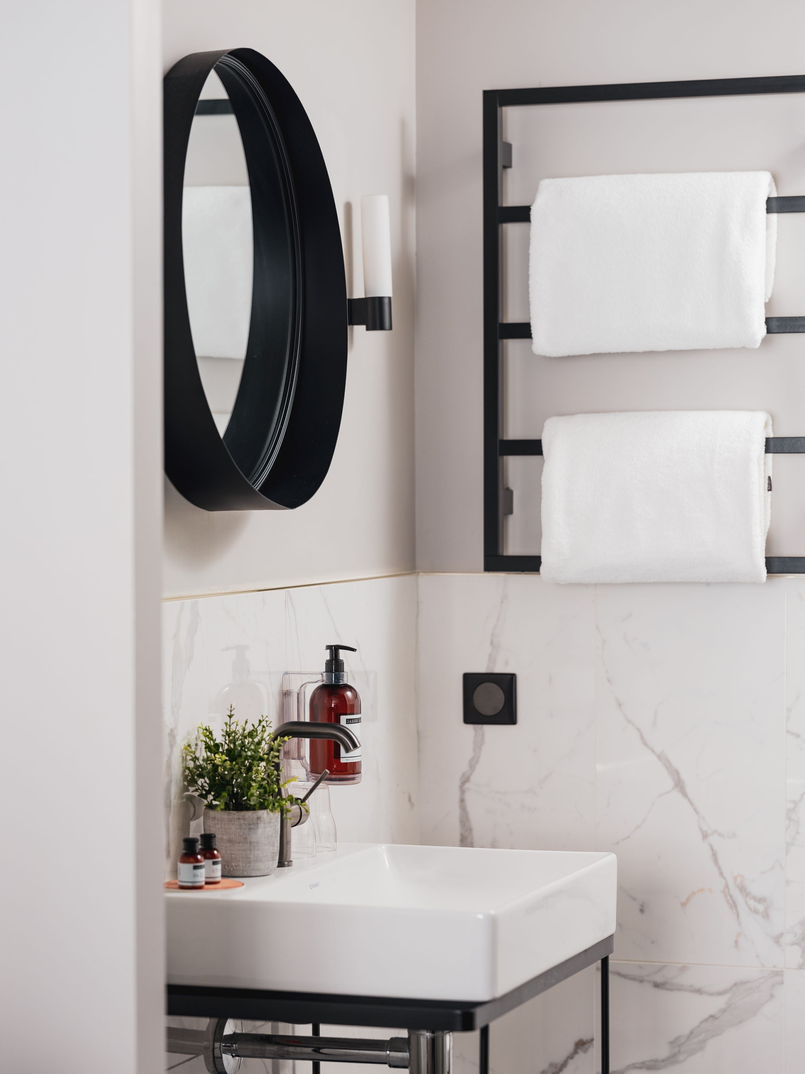 A modern bathroom with a white sink, black fixtures, a round mirror, and two white towels on a rack.