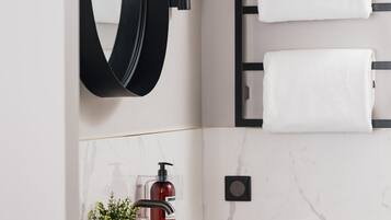 A modern bathroom with a white sink, black fixtures, a round mirror, and two white towels on a rack.