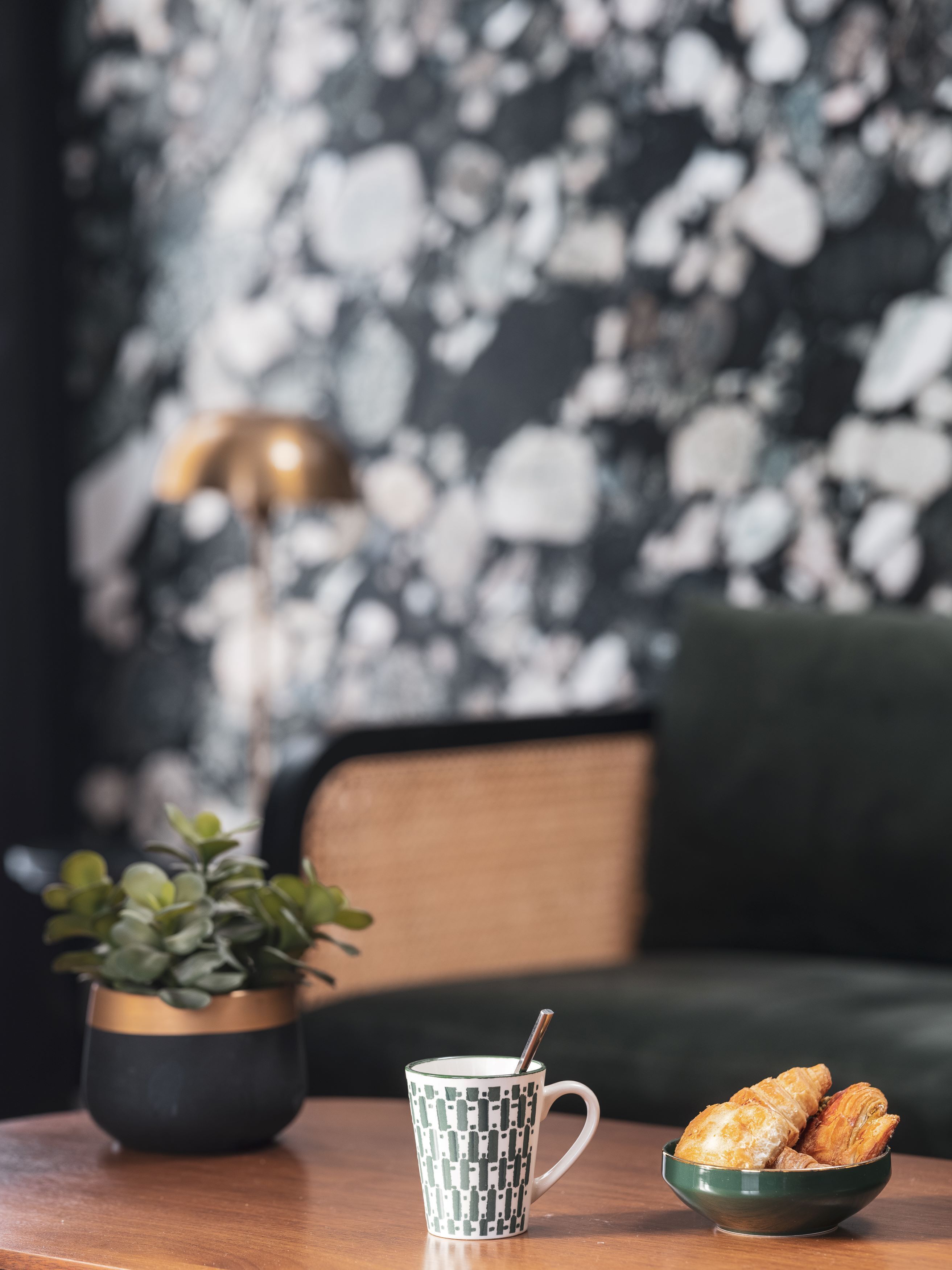 Une table avec une tasse à motifs, un bol de croissants et une plante en pot.
