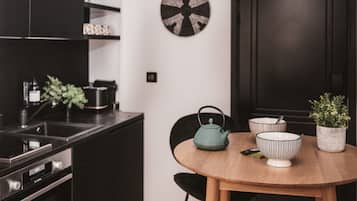 A modern kitchen with a round wooden table, a kettle, bowls, and a potted plant.