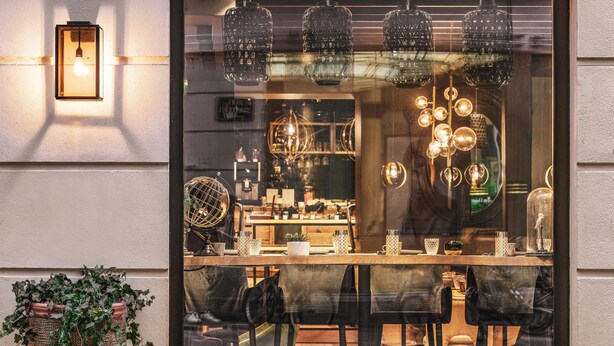 Un restaurante con un amplio ventanal, luces colgantes y una planta en maceta afuera.