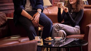 A man and a woman sitting on a leather couch in a room with wooden paneling and a patterned carpet. - Hôtel de l'Europe by Happyculture (Strasbourg)
