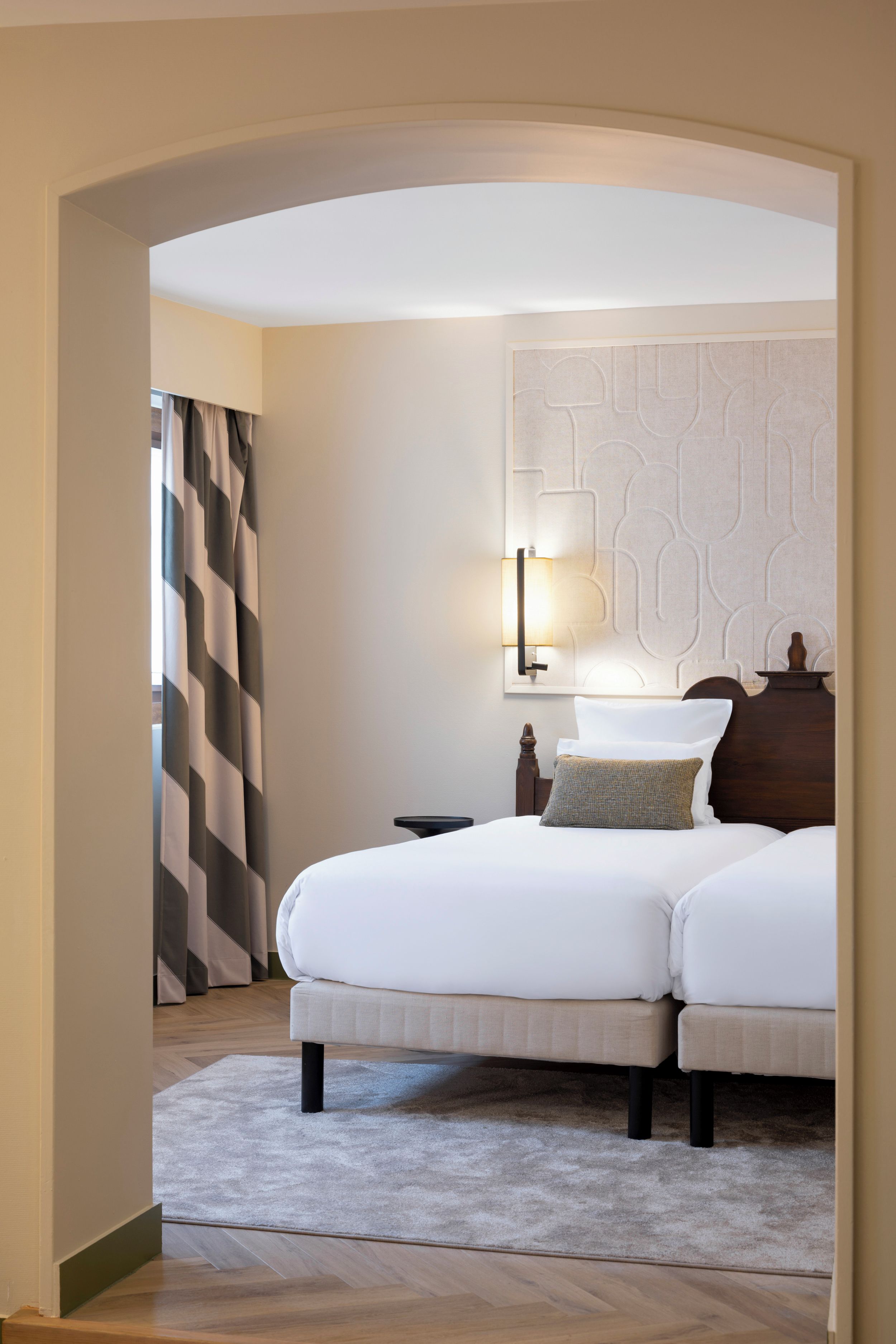 Quarto de hotel com cama, mesa de cabeceira, abajur e um painel decorativo na parede.