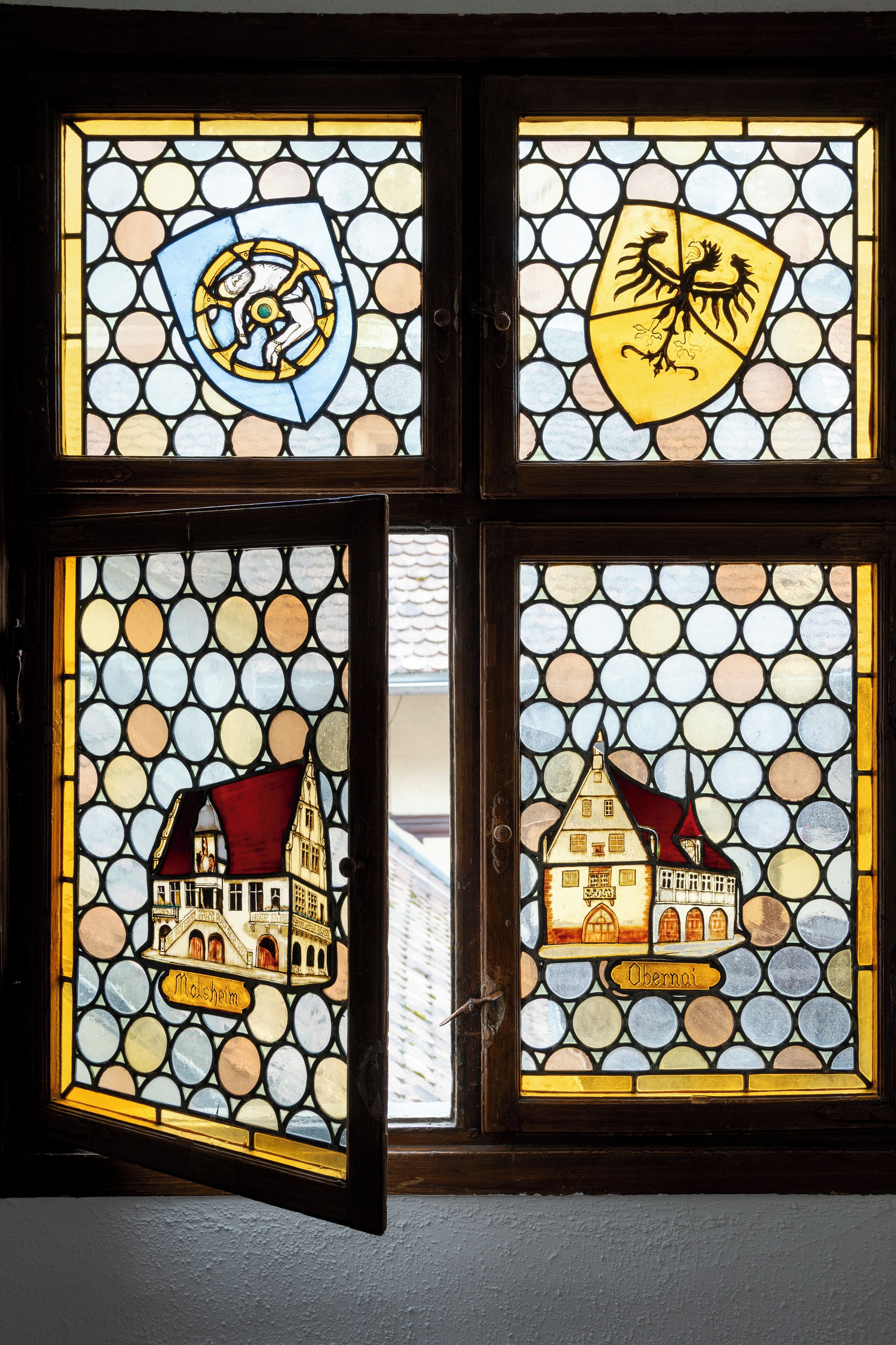 A stained glass window with four distinct panels, each depicting different scenes or symbols.