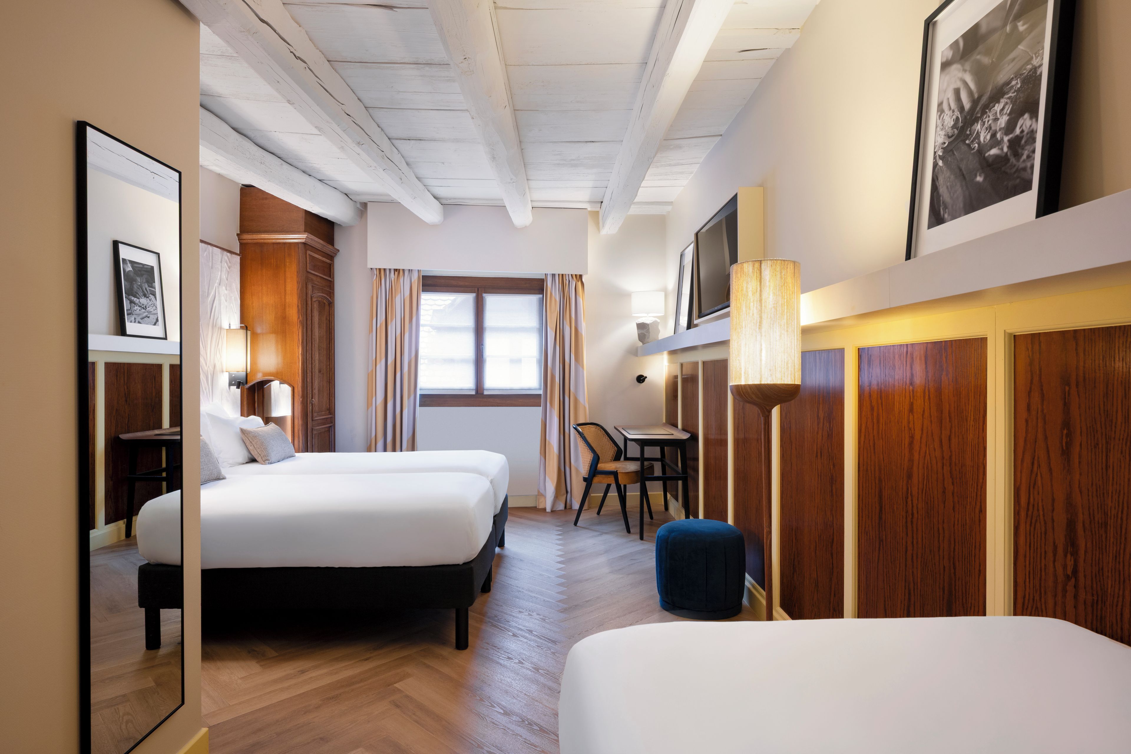 A hotel room with two beds, a desk, a chair, and a large window.