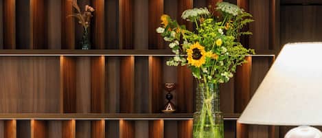 Un interno moderno con parete rivestita in legno, un vaso verde con fiori, un tavolo bianco e sgabelli decorati.